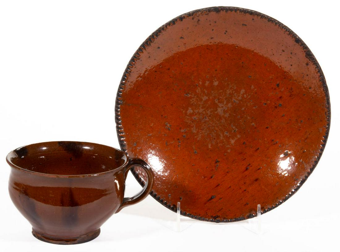 AMERICAN EARTHENWARE / REDWARE TABLE ARTICLES, LOT OF: AMERICAN EARTHENWARE / REDWARE TABLE ARTICLES, LOT OF TWO, lead-glazed, comprising a bulbous-form porringer, having strap handle with medial channel, and manganese splotches, and a 9 7/8" D plate with