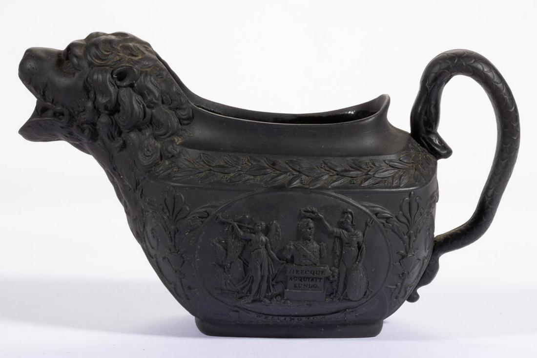 ENGLISH BLACK BASALT DRY-BODIED STONEWARE COMMEMORATIVE: ENGLISH BLACK BASALT DRY-BODIED STONEWARE COMMEMORATIVE CREAMER, having molded lionâ€™s head spout and serpent handle, commemorating Wellingtonâ€™s victories at "India / Portugal & Spain. / 