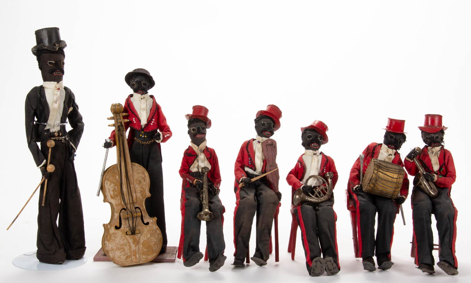 BLACK AMERICANA FOLK ART JAZZ BAND CLOTH DOLLS, SET OF: BLACK AMERICANA FOLK ART JAZZ BAND CLOTH DOLLS, SET OF SEVEN, each with stitched faces and hold instruments, comprising six in red suits, and one in black. 20th century. Black Suit 14" H. Provenance: 