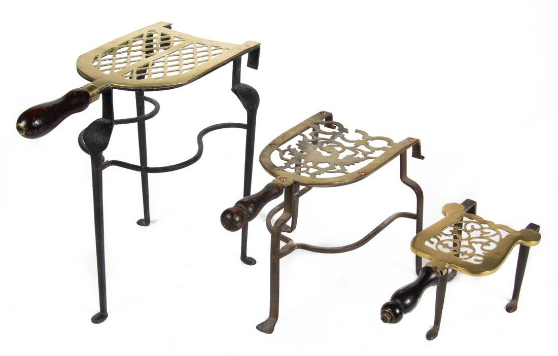 ASSORTED ENGLISH BRASS AND WROUGHT-IRON HEARTH TRIVETS,: ASSORTED ENGLISH BRASS AND WROUGHT-IRON HEARTH TRIVETS, LOT OF FOUR, various forms with brass stylized open-work patterns on a wrought-iron base raised on three tall legs with pad feet, each with hook
