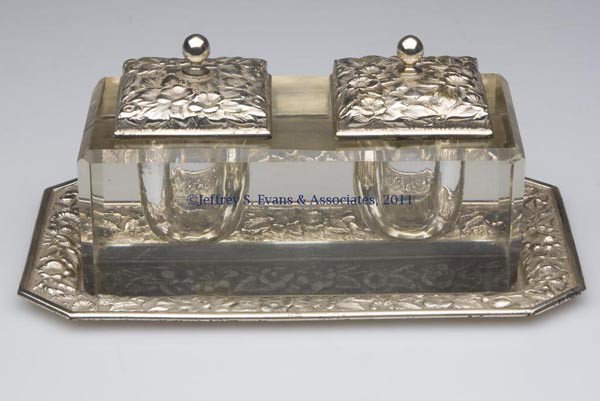 SILVER AND GLASS INKSTAND: SILVER AND GLASS INKSTAND, double-well with two plated-silver lids, resting on a tray marked "THEO. A. KOHN & SON" and "STERLING." First quarter 20th century. 3 1/2" HOA, 5 1/4" x 9" overall. Provenan