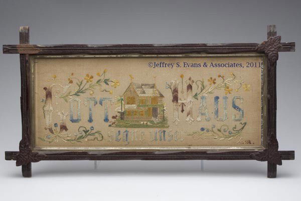 PUNCH PAPER MOTTO NEEDLEWORK FRAMED SAMPLER: PUNCH PAPER MOTTO NEEDLEWORK FRAMED SAMPLER, house surrounded by verse "GOTT SEGNE UNSER HANS" along with floral vines and initials in lower right corner, walnut cross over frame with applied leaf dec