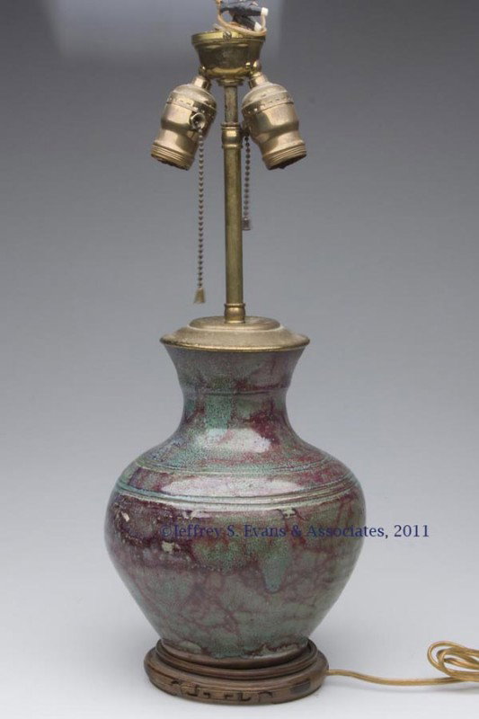 JUGTOWN WARE VASE LAMP: JUGTOWN WARE VASE LAMP, mottled green and red glaze, bulbous form mounted on a wooden base, flared rim, impressed mark on base, electrified. Second quarter 20th century. 19" HOA, 5 1/4" D base; vase 9