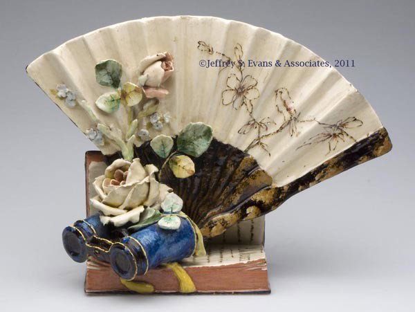 FRENCH MAJOLICA FAN-FORM VASE: FRENCH MAJOLICA FAN-FORM VASE, decorated with applied opera glasses and flowers, resting on an open book inscribed "A. de MUSSET," unmarked. Fourth quarter 19th century. 9 1/2" H, 13" W.