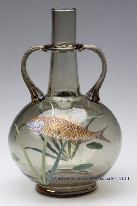 MOSER-STYLE DECORATED GLASS HANDLED BOTTLE: MOSER-STYLE DECORATED GLASS HANDLED BOTTLE, smoky brown, featuring a well-executed fish and aquatic plant life, with two applied handles and neck ring. Late 19th/early 20th century. 7 1/2" H, 4 1/2" D