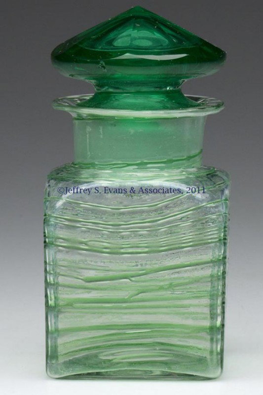 STEUBEN REEDED STOPPERED JAR: STEUBEN REEDED STOPPERED JAR, colorless jar with random green reeding, original green facet-top stopper, polished pontil mark, not signed, detached Rockwell Gallery sticker. Steuben Glass Works. First