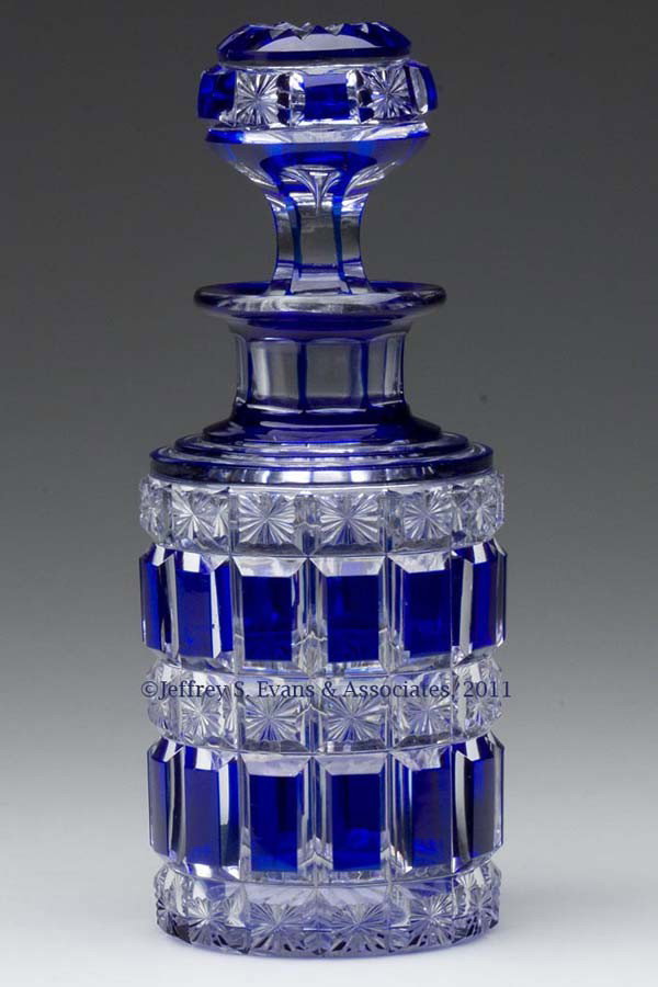 CUT OVERLAY PANEL AND STAR COLOGNE BOTTLE: CUT OVERLAY PANEL AND STAR COLOGNE BOTTLE, deep cobalt blue to colorless, cylindrical form with a stepped shoulder, short panel-cut neck, flanged mouth, and star-cut base, original air-trap stopper wi