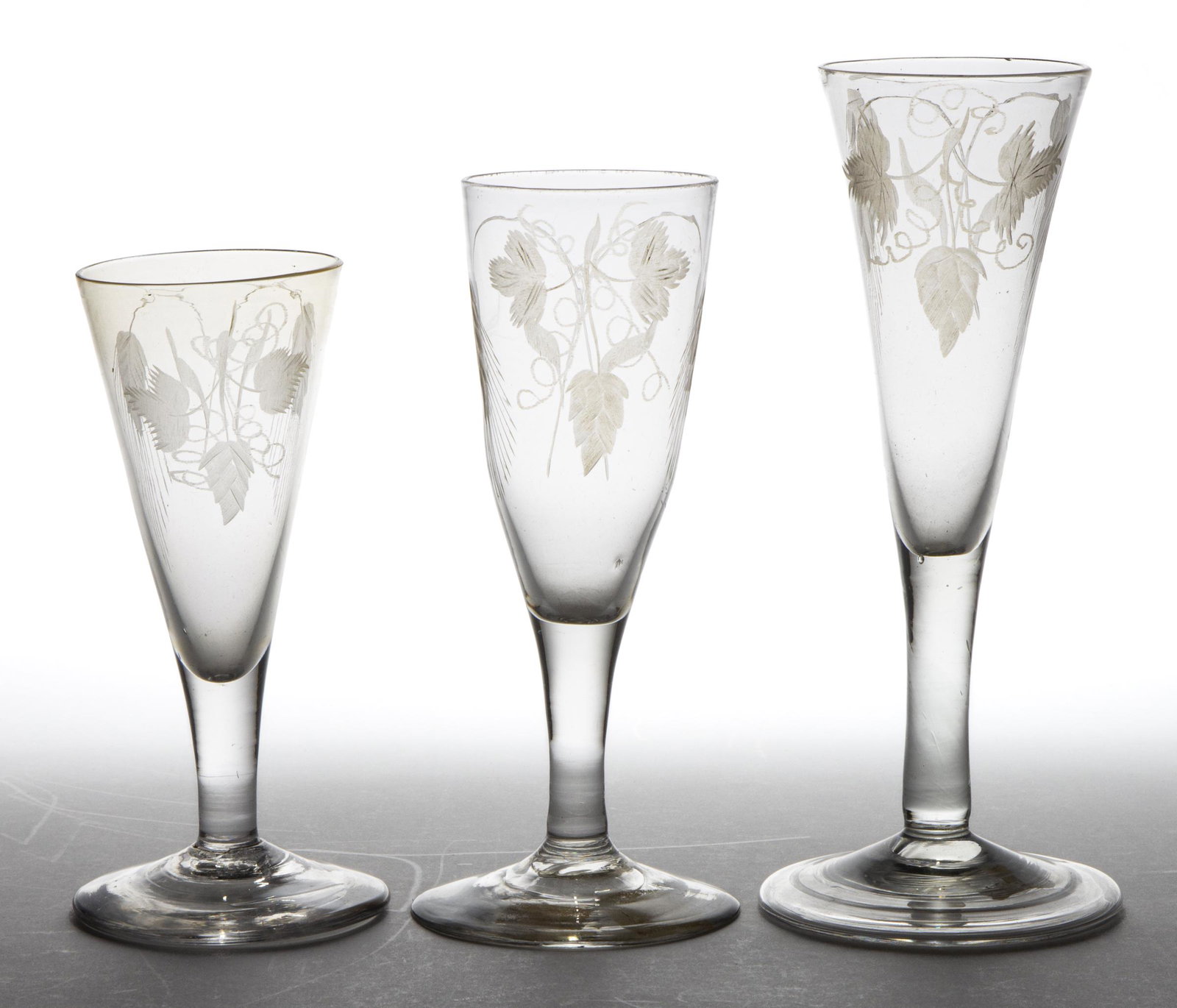 FREE-BLOWN AND ENGRAVED WINES, LOT OF THREE: FREE-BLOWN AND ENGRAVED WINES, LOT OF THREE, colorless, comprising two with conical bowls and one having a rounded funnel bowl, each having matching wheat engraved decoration, each raised on a thin st