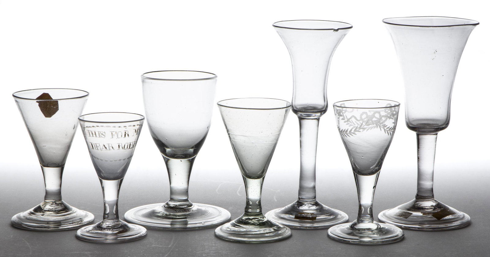 FREE-BLOWN GLASS WINES, LOT OF SEVEN: FREE-BLOWN GLASS WINES, LOT OF SEVEN, colorless, some having a green or blue tint, including two examples with engraved decoration with one stating "THIS FOR MY DEAR ROBERT", and two tall examples. Va