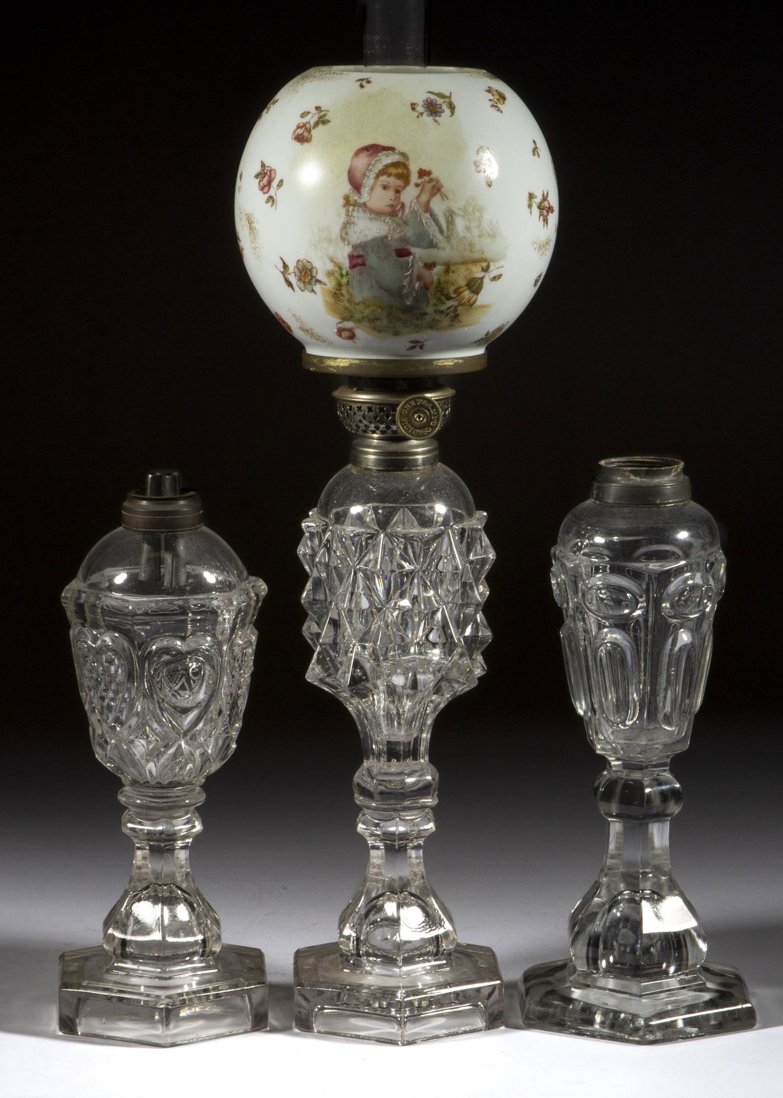 ASSORTED FLINT EAPG WHALE OIL / FLUID STAND LAMPS, LOT OF THREE: ASSORTED FLINT EAPG WHALE OIL / FLUID STAND LAMPS, LOT OF THREE, colorless lead glass, comprising a Giant Sawtooth topped with an opaque white ball shade featuring a Victorian child, a Heart, and a Ci