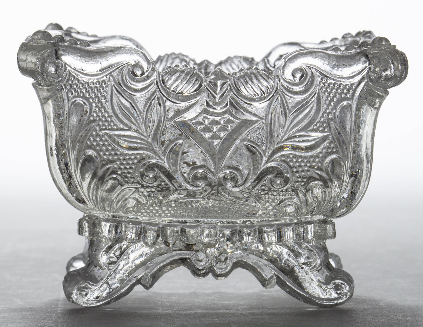 PE-1 PROVIDENCE MARKED PRESSED OPEN SALT: PE-1 PROVIDENCE MARKED PRESSED OPEN SALT, colorless, eagle-headed shield on each end, "PROVIDENCE" in base, raised on four scrolled feet. Very rare. Providence Flint Glass Co. 1835-1850. 2 1/4" H, 2 3