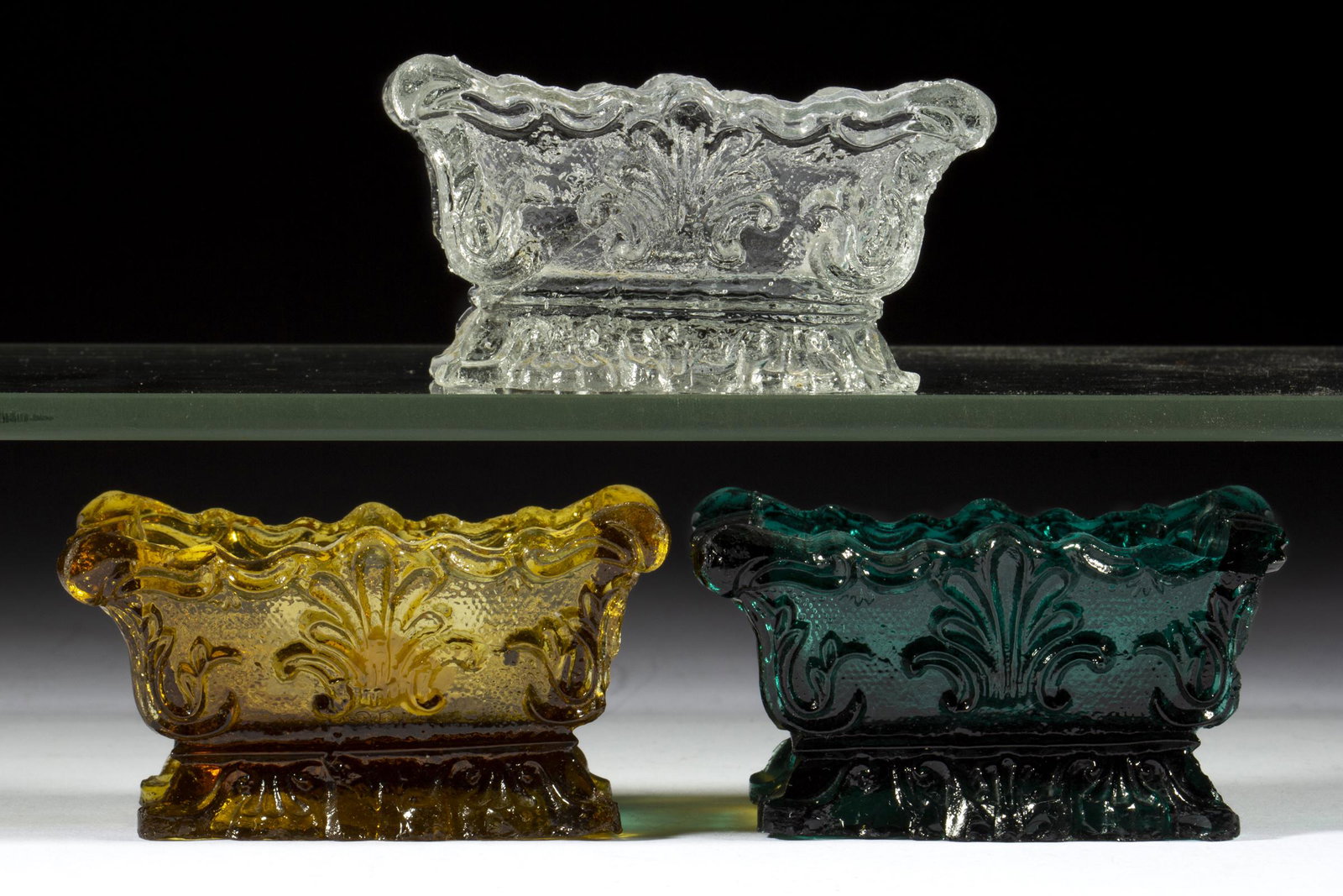 SL SHELL PRESSED OPEN SALTS, LOT OF THREE: SL SHELL PRESSED OPEN SALTS, LOT OF THREE, comprising a green SL-1, an amber SL-1a variant with a 4x9 diamond base, and a colorless SL-1a. Scarce and extremely rare. Probably Boston & Sandwich Glass C