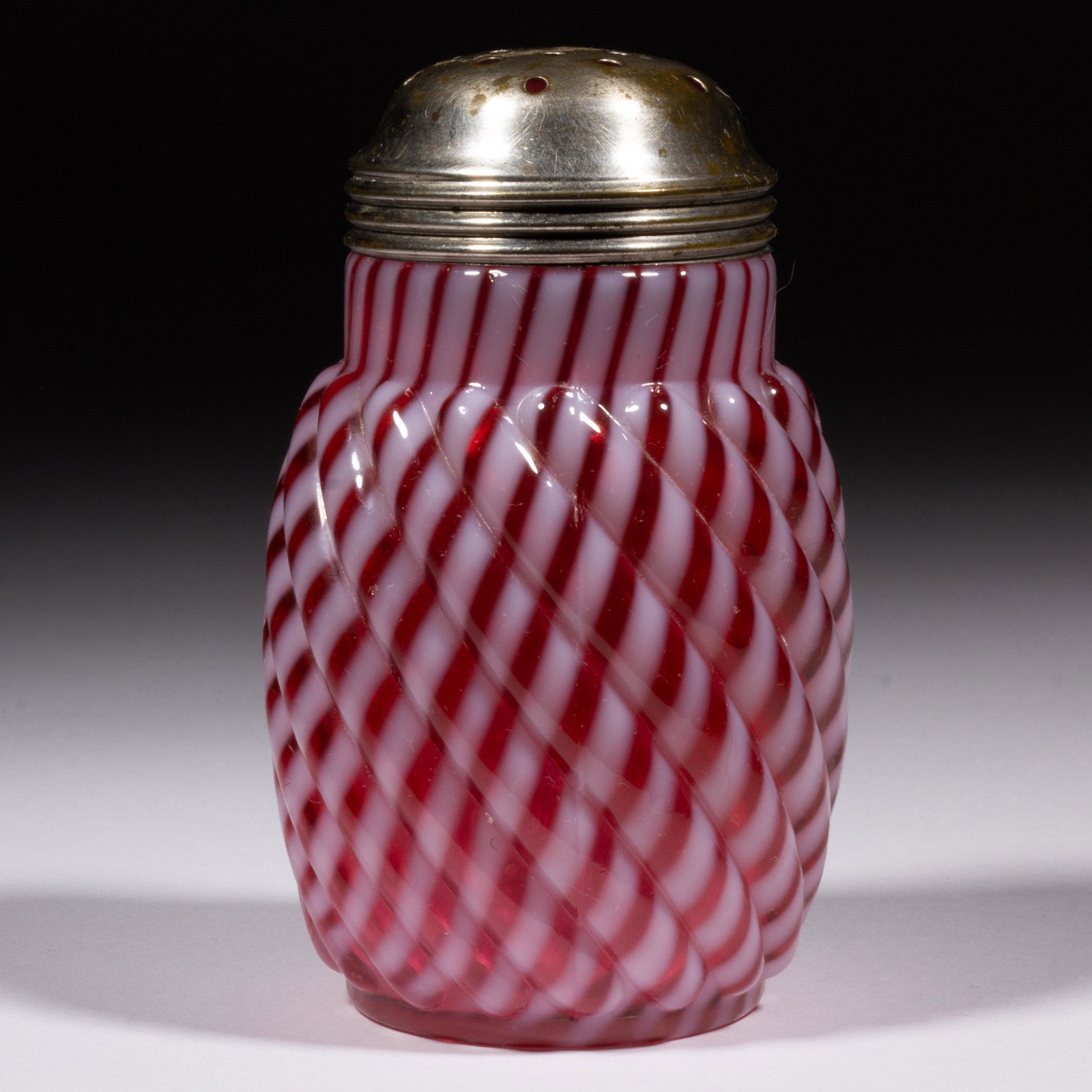 REVERSE SWIRL SUGAR SHAKER,: REVERSE SWIRL SUGAR SHAKER, cranberry opalescent, period lid. Maker unverified. 1888-1902. 4 3/4" H. Literature: Heacock/Elmore - Opalescent Glass From A-Z, p. 164, fig. 716. Provenance: The Dean & Le