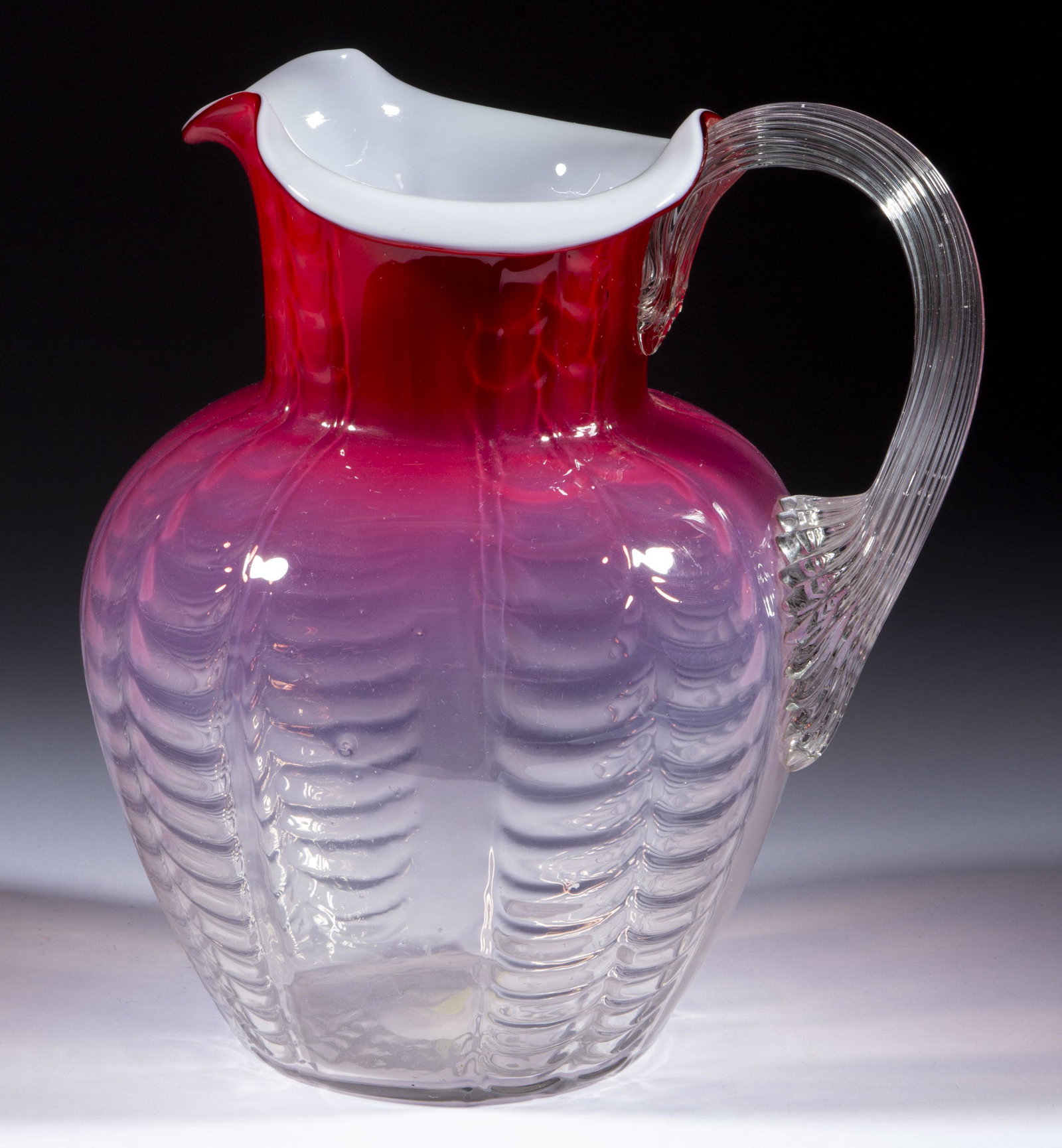 VICTORIAN DRAPED COLUMNS OPALESCENT WATER PITCHER,: VICTORIAN DRAPED COLUMNS OPALESCENT WATER PITCHER, shaded cranberry opalescent to colorless, shouldered form, applied colorless reeded handle, polished pontil mark. Maker unverified. Late 19th/early 2