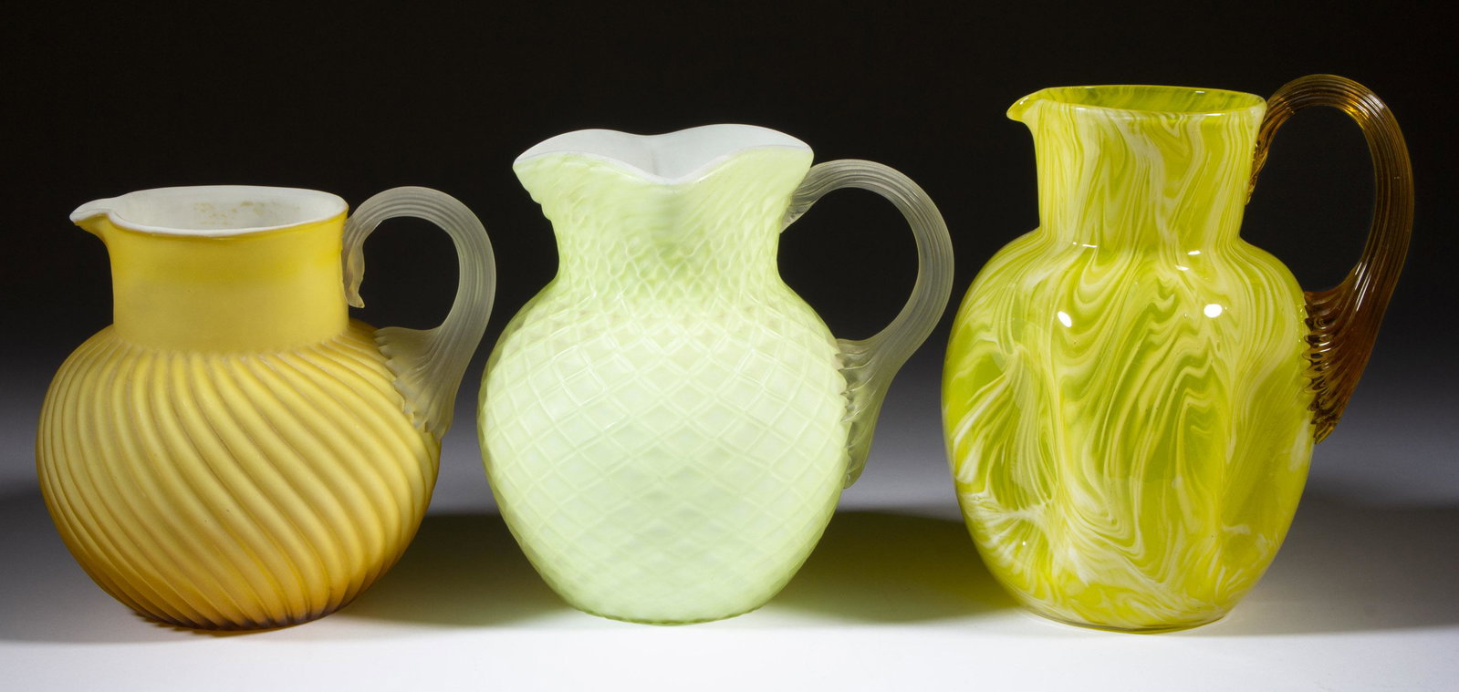 ASSORTED VICTORIAN GLASS PITCHERS, LOT OF THREE,: ASSORTED VICTORIAN GLASS PITCHERS, LOT OF THREE, comprising a cased lemon Diamond-Quilt, an satin amber to opaque white Swirl, and a dimpled yellow and opal pitcher, each having an applied reeded hand