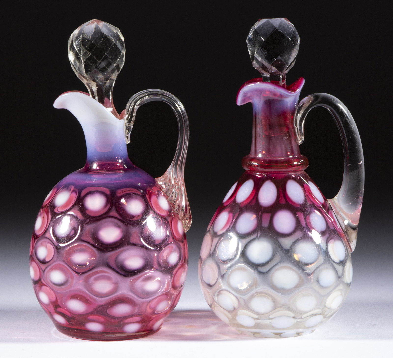 VICTORIAN COINSPOT OPALESCENT GLASS CRUETS, LOT OF TWO,: VICTORIAN COINSPOT OPALESCENT GLASS CRUETS, LOT OF TWO, comprising a cranberry opalescent globular, and a rubina opalescent Ring-Neck, each having an applied handle and a pressed-faceted stopper. Vari