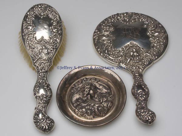 UNGER BROTHERS STERLING SILVER DRESSER ARTICLES, L: UNGER BROTHERS STERLING SILVER DRESSER ARTICLES, LOT OF THREE, comprising a Cupid hand mirror and brush, non-matching monograms; and a She Loves Me pin tray. Fully marked. Fourth quarter 19th to early