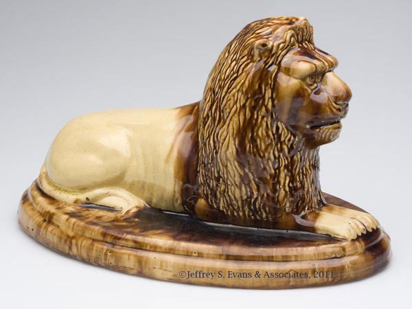 ROCKINGHAM-GLAZE POTTERY RECUMBENT LION FIGURE / D: ROCKINGHAM-GLAZE POTTERY RECUMBENT LION FIGURE / DOORSTOP, mottled brown, hollow, well-molded figure, on an oval base, unmarked. United States, possibly Ohio. Second half 19th century. 8 1/2" HOA, 9" 