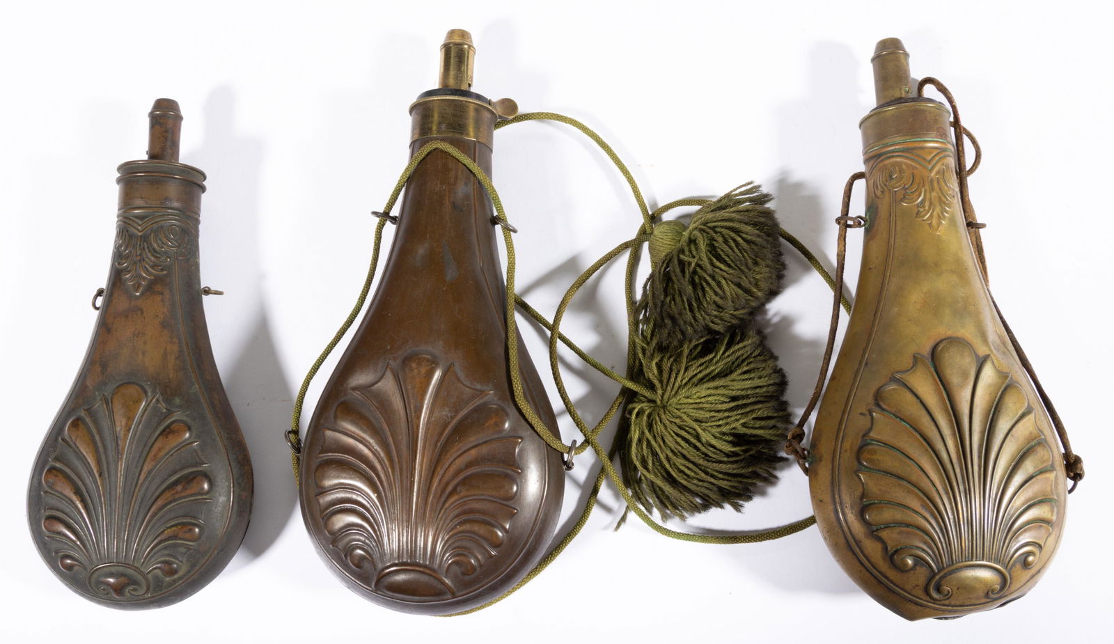 ASSORTED EMBOSSED BRASS / COPPER POWDER FLASKS, LOT OF THREE,: each with shell design to both sides and original hanging loops. Large brass example marked for the American Flask & Cap Co., larger copper example marked for James Dixon & Sons, Sheffield. Second hal