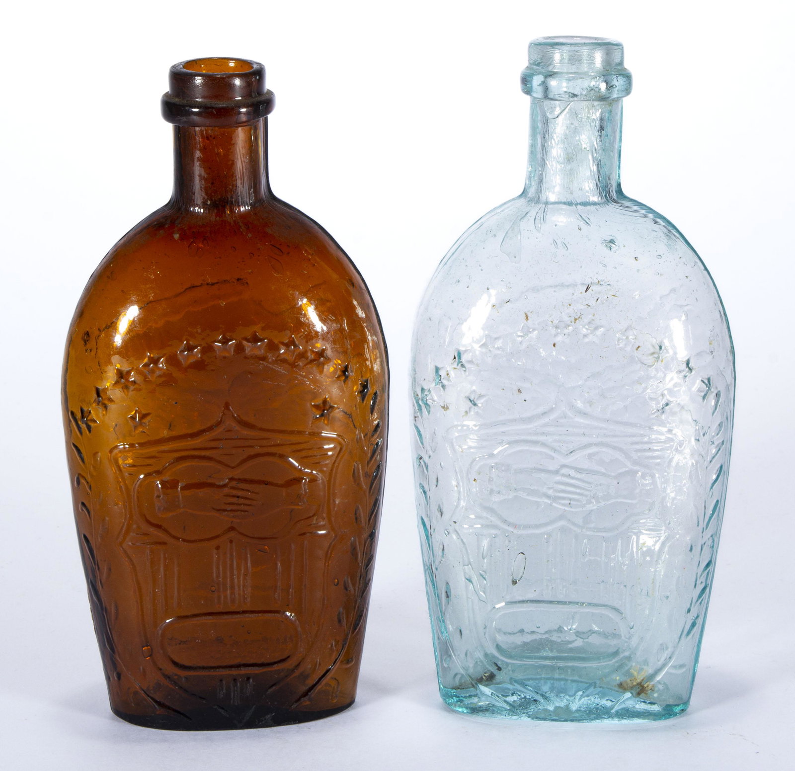 GXIII-31 CLASPED ARMS / EAGLE HISTORICAL FLASKS, LOT OF TWO,: aquamarine and deep amber, each half-pint with an applied lip and plain base. Midwestern. 1860-1880. 6 1/4" and 6 1/2" H.Provenance: From the Eddie Tatum estate collection, Winston-Salem, NC.