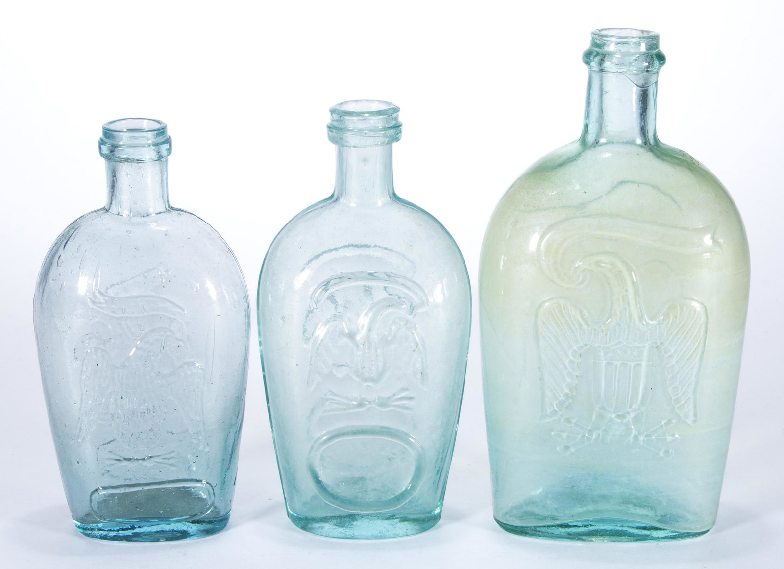 ASSORTED EAGLE HISTORICAL FLASKS, LOT OF THREE,: comprising a light green pint GII-118, a blue-green half-pint GII-128, and an aquamarine half-pint GII-109, each having an applied lip and plain base. Pittsburgh area. 1860-1880. 6" to 7 1/4" H.Proven