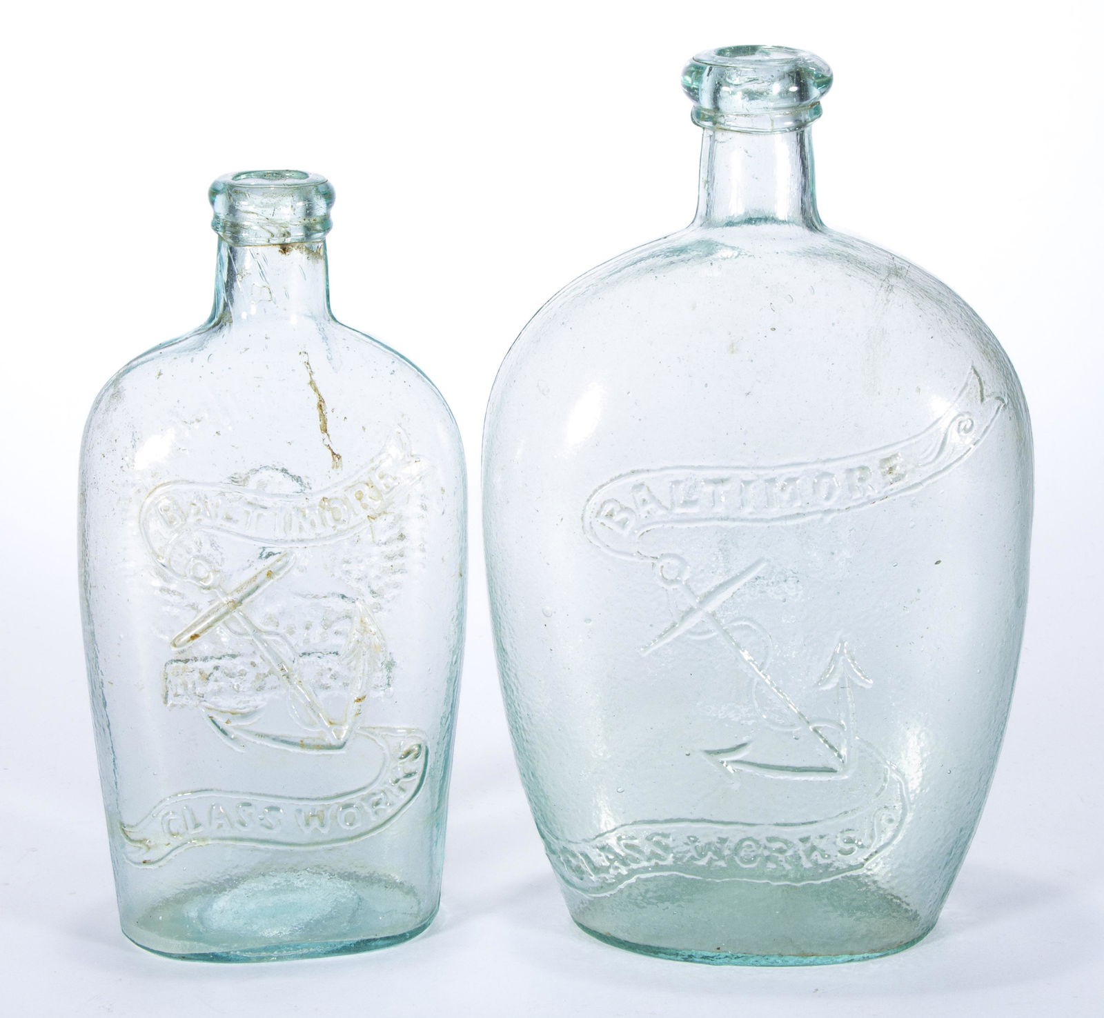 ASSORTED BALTIMORE GLASS WORKS HISTORICAL FLASKS, LOT OF TWO,: comprising a light green quart GXIII-48 and an aquamarine GXIII-53 pint, each having an applied lip and a plain base. Baltimore, MD. 1860-1880. 7 3/4" to 8 3/4" H.Provenance: From the Eddie Tatum esta