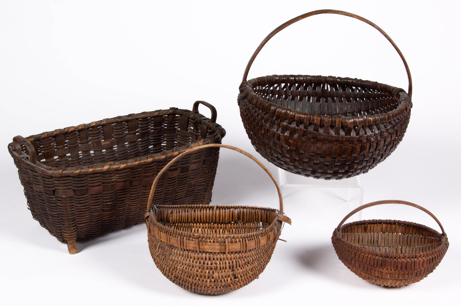APPALACHIAN AND OTHER BASKETS, LOT OF FOUR,: ash and white oak splint, comprising a rectangular example with end handles and four short feet, a half-kidney wall example, and two melon forms. Large example with old varnished surface, others with 