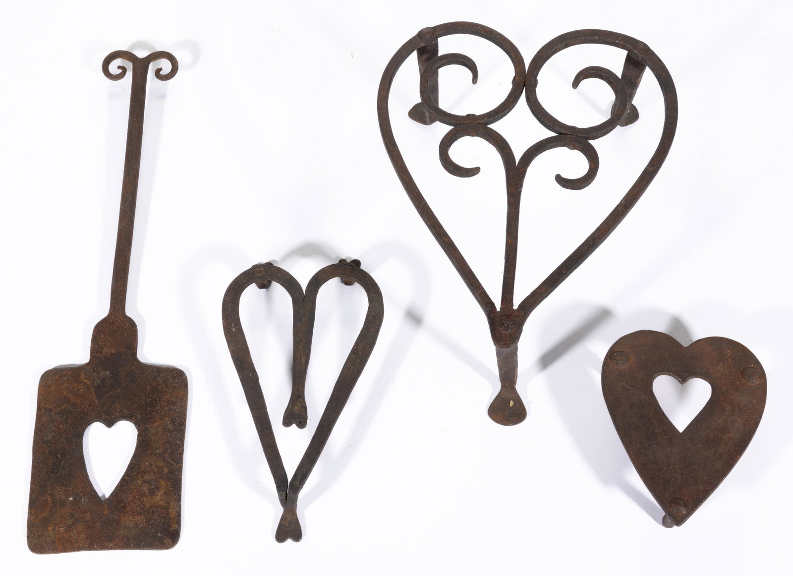 ASSORTED WROUGHT-IRON HEART-FORM HEARTH ARTICLES, LOT OF FOUR,: comprising three trivets, one with additional heart-form feet, and a spatula with ram's-horn terminal. 19th century. Largest 4 1/2" H, 10" x 8 3/8". Provenance: From an important Roanoke, VA private c