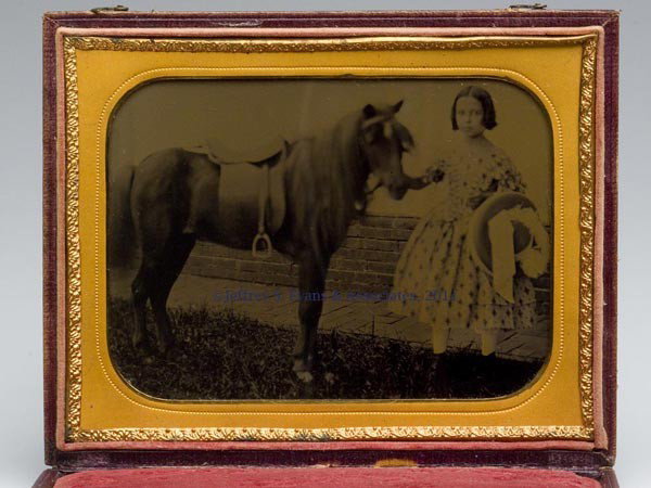LITTLE GIRL WITH PONY HALF-PLATE AMBROTYPE: LITTLE GIRL WITH PONY HALF-PLATE AMBROTYPE, outdoor setting at a brick sidewalk. Leather-covered wood snap case embossed with a central lyre. Mid 19th century. 6" x 4 3/4" case. Provenance: Pennsylva