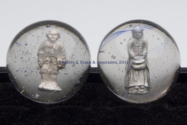 TWO HUMAN FIGURE SULPHIDE MARBLES: TWO HUMAN FIGURE SULPHIDE MARBLES, depicting a standing boy with a light pontil mark and a standing girl with hands in front pocket and a light blue striation. Late 19th/early 20th century. 1 5/8" and