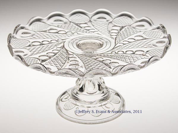 HORN OF PLENTY SALVER / CAKE STAND: HORN OF PLENTY SALVER / CAKE STAND, colorless lead glass, plate with a slightly up-turned 18-scallop rim, raised on a six-lobe stem and circular foot with the pattern repeated underneath, wafer constr