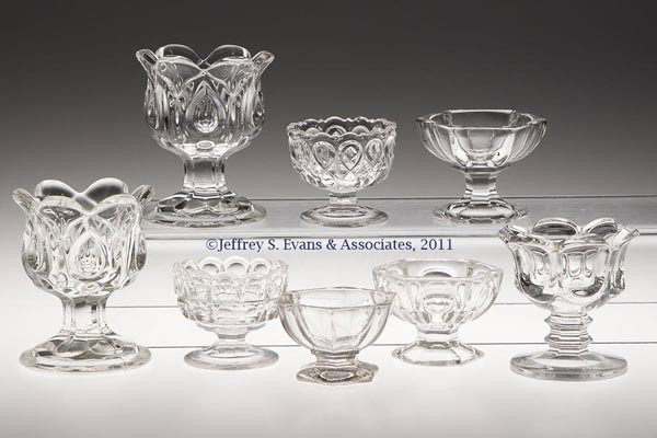 VARIOUS PRESSED SALTS, LOT OF EIGHT: VARIOUS PRESSED SALTS, LOT OF EIGHT, colorless lead glass, each raised on a foot. Third quarter 19th century. Various sizes. Provenance: Personal collection of Judith (Judy) Cronin, Orleans, MA.