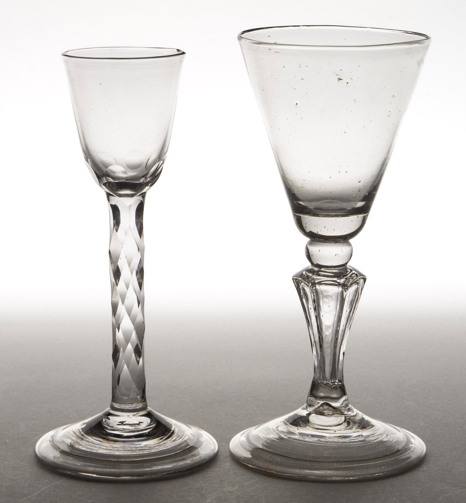 FREE-BLOWN GLASS WINES, LOT OF TWO: FREE-BLOWN GLASS WINES, LOT OF TWO, colorless, comprising one with a round funnel bowl with a cut-faceted stem, and a molded pedestal wine having a conical bowl. (UPDATED 11/8/2022) European. 18th cen