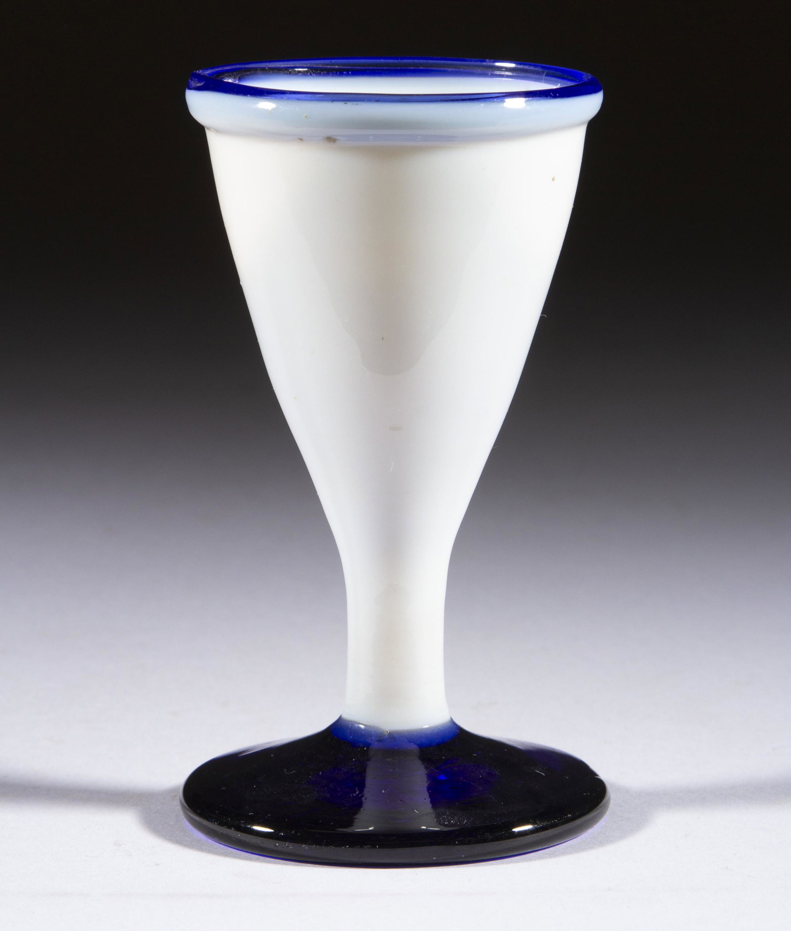 FREE-BLOWN OPAQUE GLASS WINE: FREE-BLOWN OPAQUE GLASS WINE, opal/opaque white with applied cobalt blue rim, tapered form with an applied deep cobalt blue foot, rough pontil mark. Maker unverified. First half 19th century. 3 3/4" H