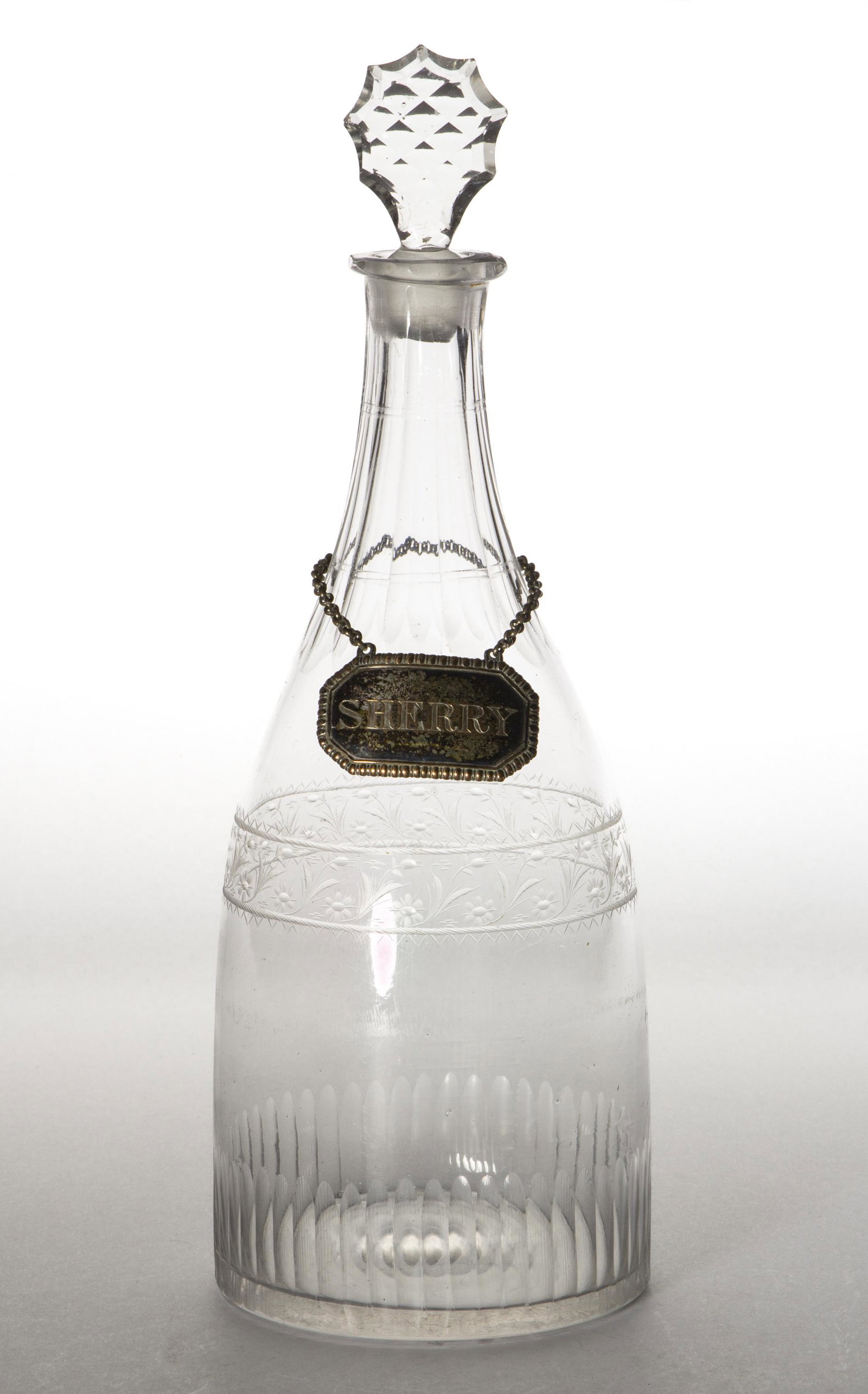 FREE-BLOWN AND ENGRAVED GLASS DECANTER: FREE-BLOWN AND ENGRAVED GLASS DECANTER, colorless, Prussian form with cut flutes to the neck, medial floral band, prism basal cuts, fitted with a silver-plate "SHERRY" tag, period cut-faceted stopper.