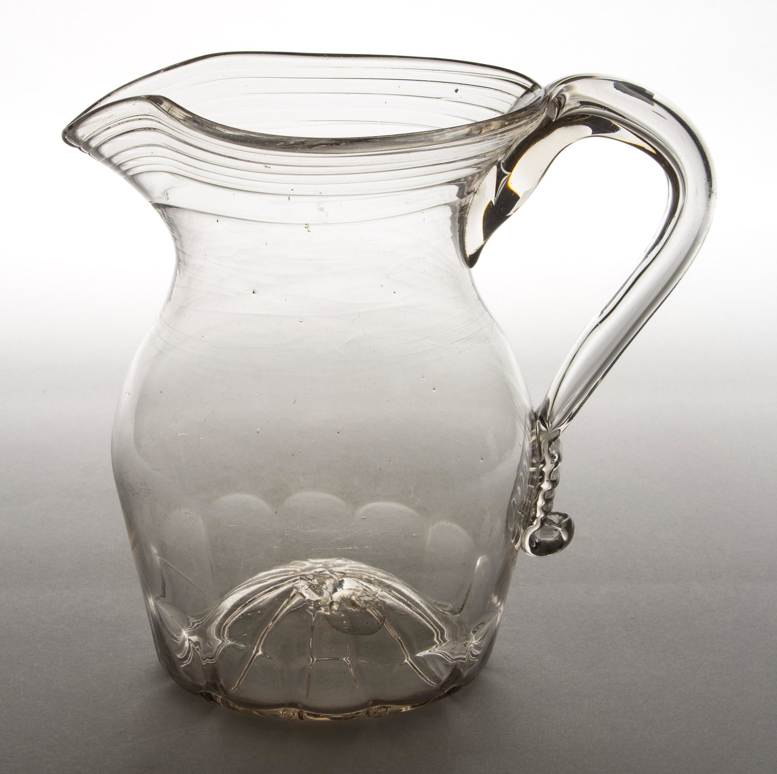 PATTERN-MOLDED GLASS PITCHER: PATTERN-MOLDED GLASS PITCHER, colorless with a light pink tint, baluster form with 12 basal flutes, tooled rim, applied hollow handle, kick-up base with a rough pontil mark. Pittsburgh area. 1815-1840