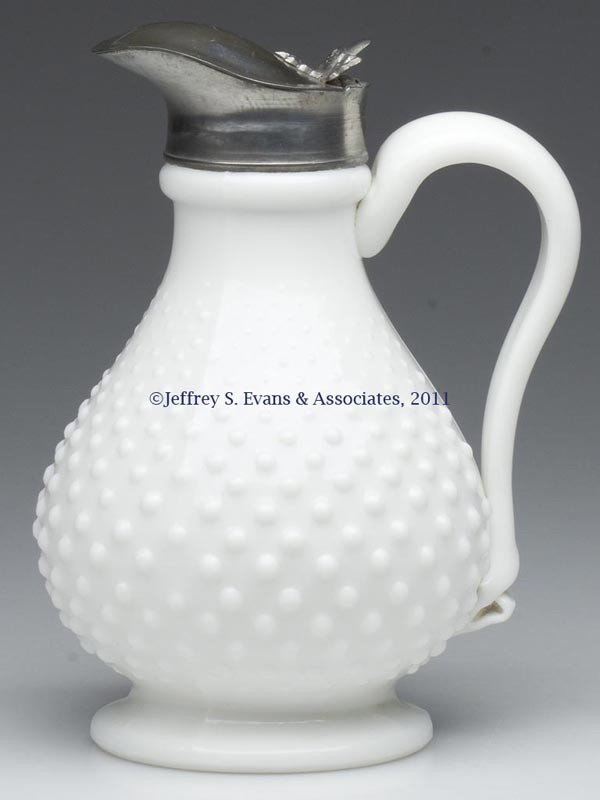 BLOWN-MOLDED HOBNAIL MOLASSES CAN / JUG: BLOWN-MOLDED HOBNAIL MOLASSES CAN / JUG, opaque white/milk glass, bulbous pyriform body with an applied solid handle, raised on a pronounced foot with a plain base. Original Britannia hinged lid with 