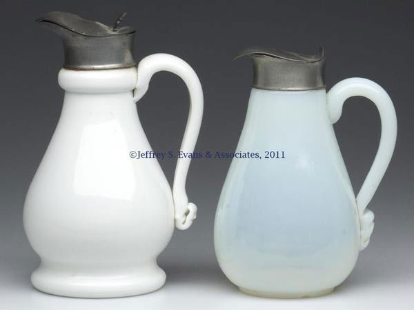 TWO BLOWN-MOLDED UNPATTERNED MOLASSES CANS / JUGS: TWO BLOWN-MOLDED UNPATTERNED MOLASSES CANS / JUGS, fiery opalescent and opaque white/milk glass, each with an applied handle, white example with a 10-petal rosette base. Original Britannia hinged lids