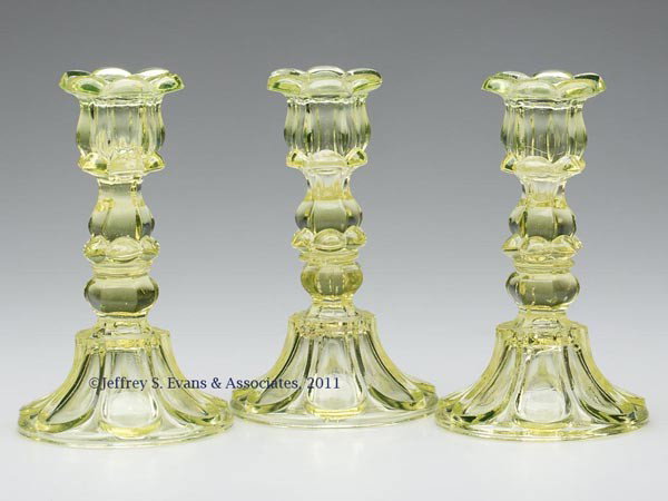 THREE PRESSED PETAL AND LOOP CANDLESTICKS: THREE PRESSED PETAL AND LOOP CANDLESTICKS, matching canary yellow, each six-petal socket with a hexagonal extension, raised on a hexagonal knop and seven-loop circular base with rough pontil mark, waf