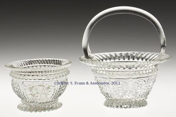 TWO GV-24 ROUND FOOTED MOLDED SALTS: TWO GV-24 ROUND FOOTED MOLDED SALTS, colorless, one with a flared rim and applied handle, each with a rough pontil mark. 19th century. 4" HOA, 4" D rim, and 2" H, 2 7/8" D rim.