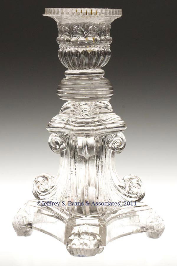 PRESSED LACY SOCKET CANDLESTICK: PRESSED LACY SOCKET CANDLESTICK, colorless, number 2 lily socket with tiny-scallop rim, raised on a complex triangular C-scroll base terminating in paw feet, compressed beehive wafer construction. Fac