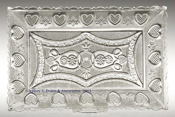 PRESSED LACY HEART UNDERTRAY: PRESSED LACY HEART UNDERTRAY, colorless, scallop and point rim, rope table ring. Boston & Sandwich Glass Co. 1835-1845. 4 1/2" x 7". Literature: B & K III, fig. 3249. Provenance: Collection of Tom Hei