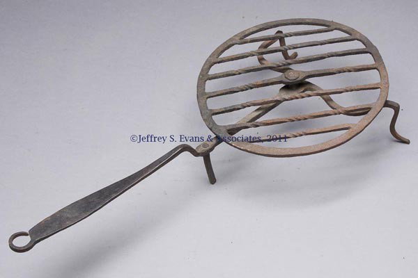 WROUGHT-IRON BROILER: WROUGHT-IRON BROILER, revolving flat ring with welded twisted crossmembers, attached by a rivet to the handle, which is split to form the two graceful front legs, third leg attached to handle just bef