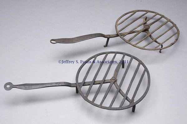 TWO WROUGHT-IRON BROILERS: TWO WROUGHT-IRON BROILERS, each with a revolving flat ring with welded straight crossmembers, attached by a rivet and washer to the handle, which is split to form the two front legs, and having a thir
