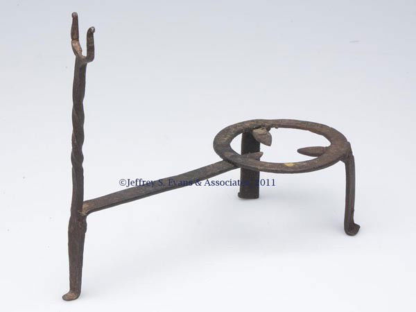 DIMINUTIVE WROUGHT-IRON TRIVET: DIMINUTIVE WROUGHT-IRON TRIVET, with handle support on an extended leg, and a flattened ring, with scallop-and-point edge, is raised on two legs which transition into central supports. Handle support