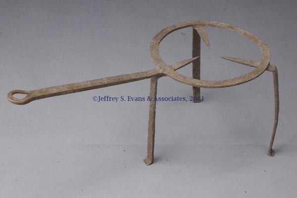 WROUGHT-IRON TRIVET: WROUGHT-IRON TRIVET, flat ring raised on three flattened legs, which transition into central supports, handle ending in a loop, slightly out-turned feet. 18th or 19th century. 11" HOA, 9 1/4" D ring,