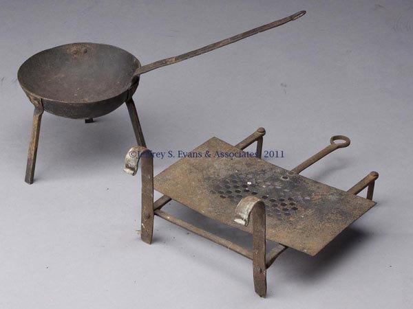 TWO IRON DOMESTIC ARTICLES: TWO IRON DOMESTIC ARTICLES, comprising a three-leg long-handle pan and a an adjustable kettle trivet with hooks to fit over a fender. Trivet: first half 19th century; pan: 19th or 20th century. Trivet