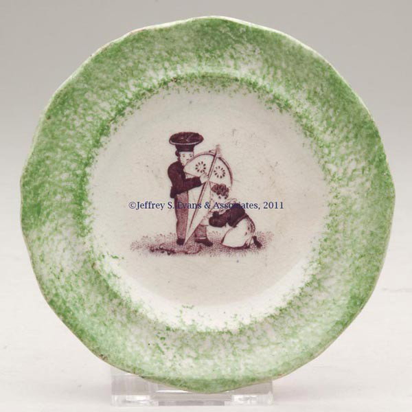 STAFFORDSHIRE TRANSFERWARE CUP PLATE: STAFFORDSHIRE TRANSFERWARE CUP PLATE, brown transfer with green sponge-decorated paneled rim, depicting two boys stringing a kite, unmarked. England. First half 19th century. 3 1/2" D. Provenance: Col