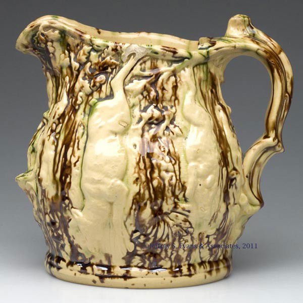YELLOW WARE FLINT ENAMEL ROCKINGHAM-TYPE GLAZE PIT: YELLOW WARE FLINT ENAMEL ROCKINGHAM-TYPE GLAZE PITCHER, mottled brown and green, body molded full-round with hanging game, and a high-relief flower under the spout. Third quarter 19th century. 9" HOA,