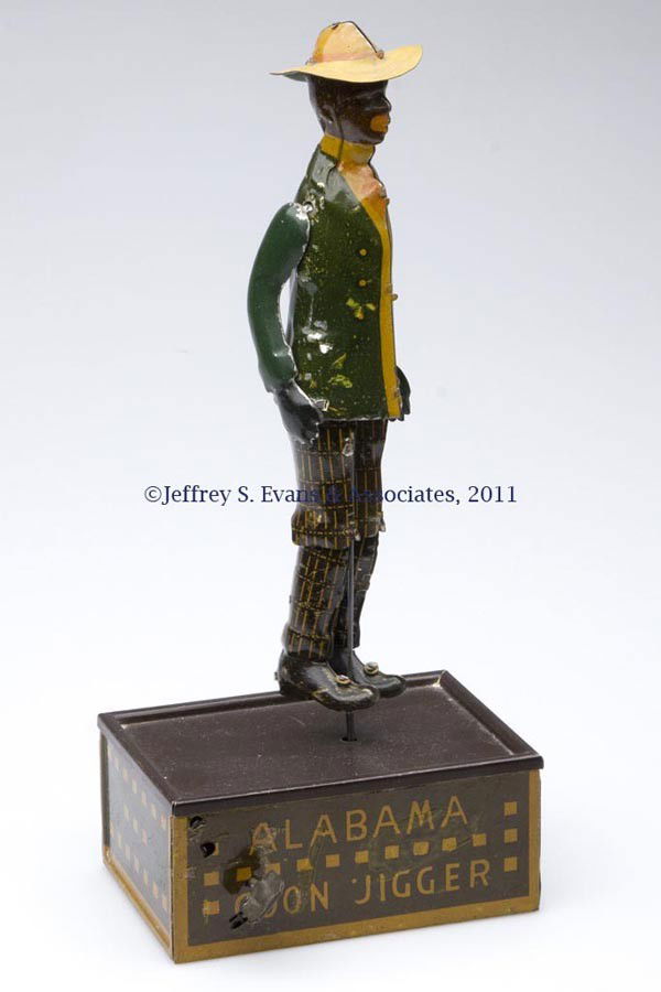 BLACK AMERICANA STRAUSS "TOMBO THE ALABAMA COON JI: BLACK AMERICANA STRAUSS "TOMBO THE ALABAMA COON JIGGER" WIND-UP TIN TOY with articulated arms and legs, green jacket and dark brown pants, dark brown-top platform with brown and yellow sides, letterin